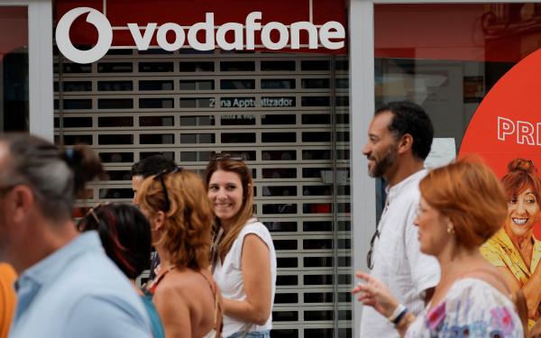 People walk past a Vodafone store in Ronda