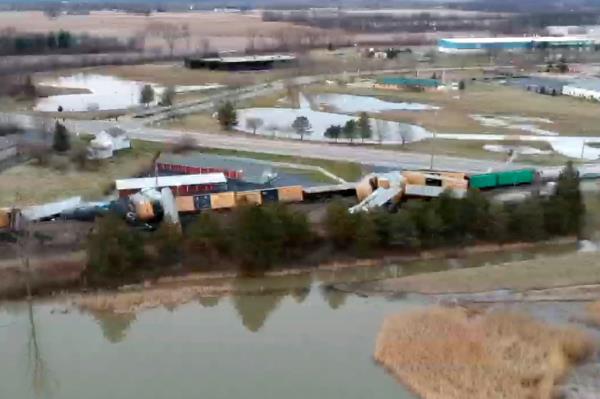 Derailed train lies next to water.