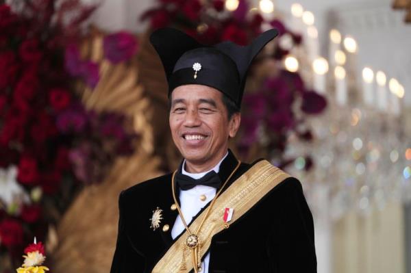 Joko Widodo. He is weaaring a traditio<em></em>nal outfit for royalty from central Java. with a white shirt, black bow tie, black jacket and gold sash. He is also wearing a black hat with extensions like ears on either side.