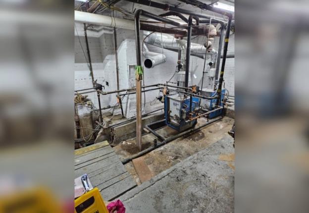 A mechanical room with machinery, boilers and an open black pipe with no cap.