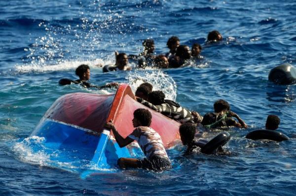 Migrants and asylum seekers swim and struggle to hold o<em></em>nto an overturned wooden boat in the Mediterranean Sea.